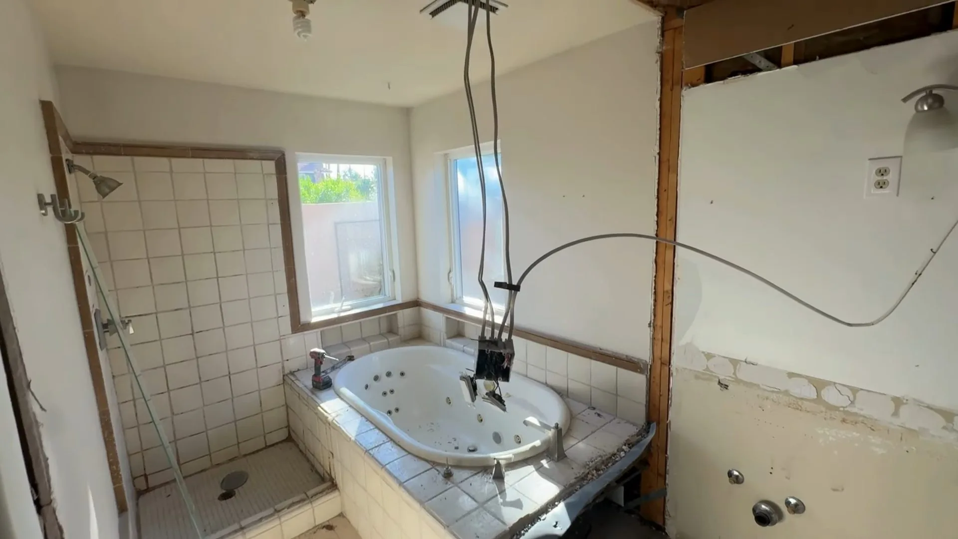 Bathroom with a section of wall removed down to the studs beside a tiled tub and shower