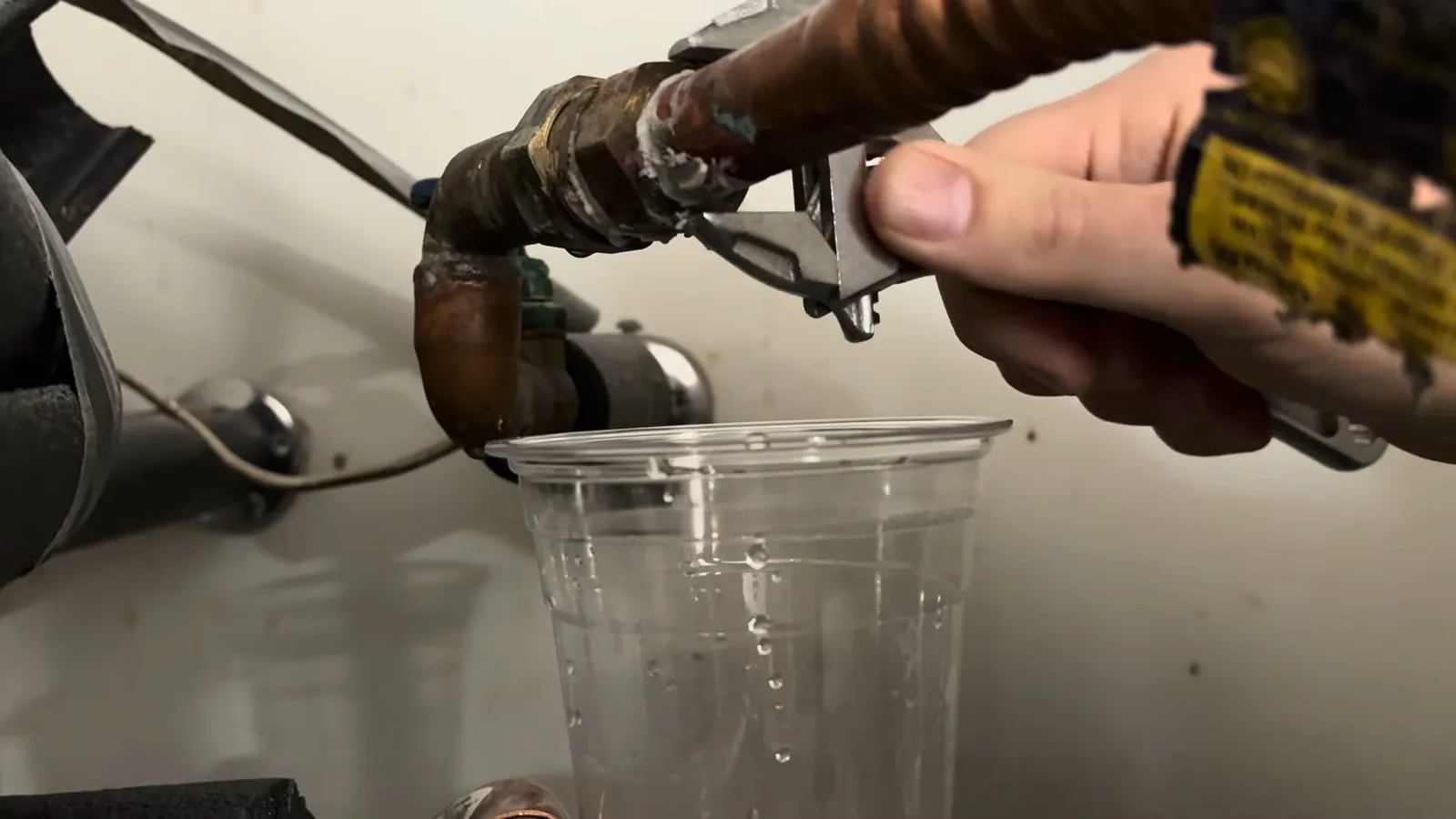 Clear plastic cup held under a water heater connection to catch water from the line