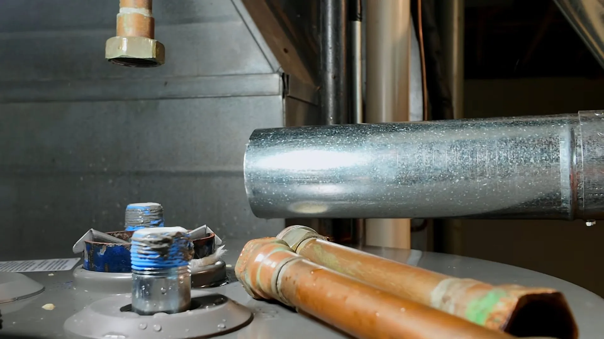 Galvanized vent pipe and two copper supply pipes rising above the top of a tank water heater