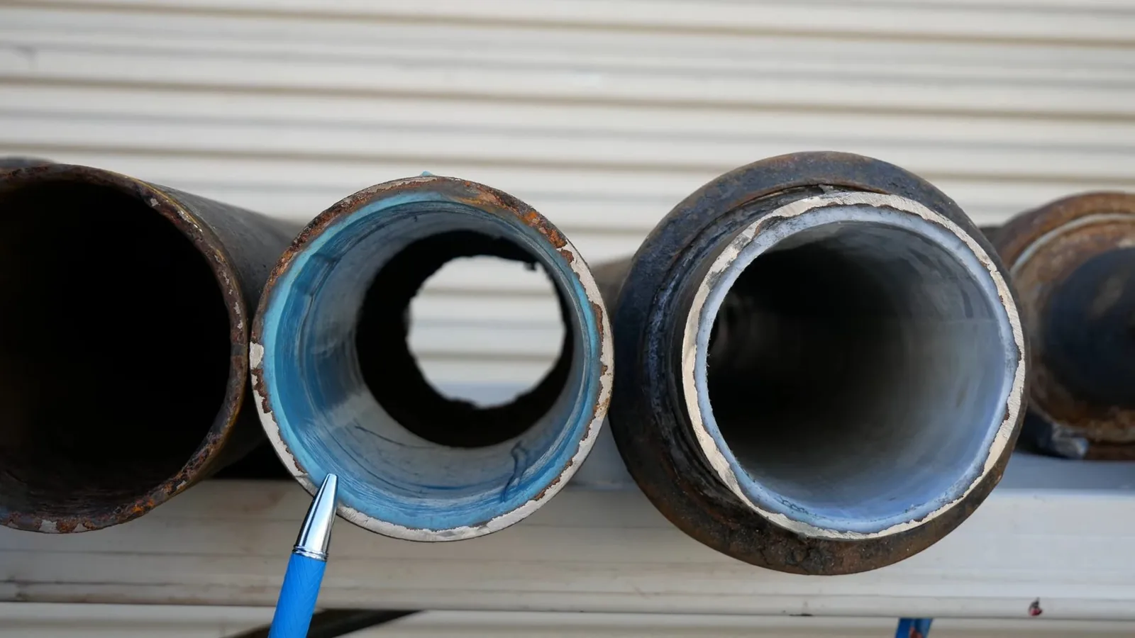 Three cut pipe sections side by side, one with a smooth blue liner inside, held by a pen