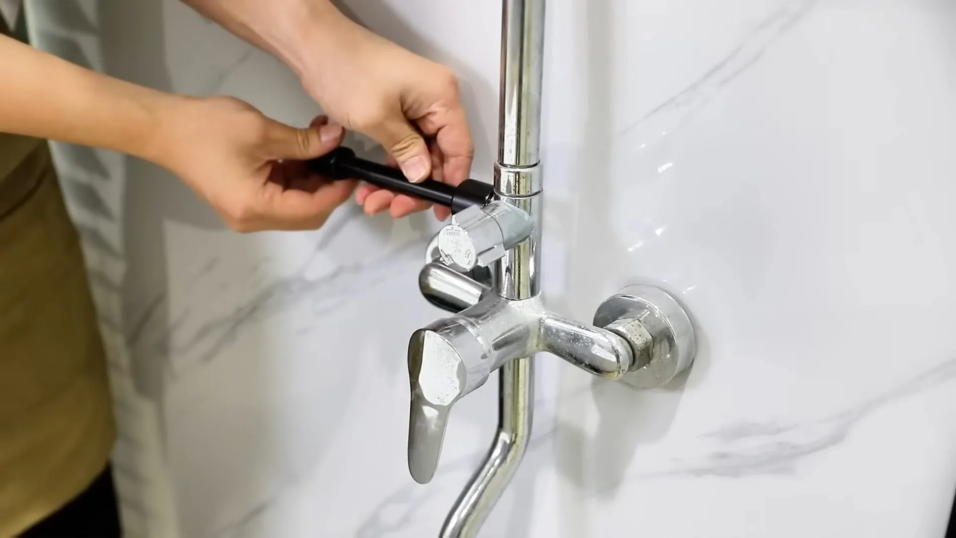Hand using a small black tool on a chrome tub and shower mixer valve mounted on a white marble wall