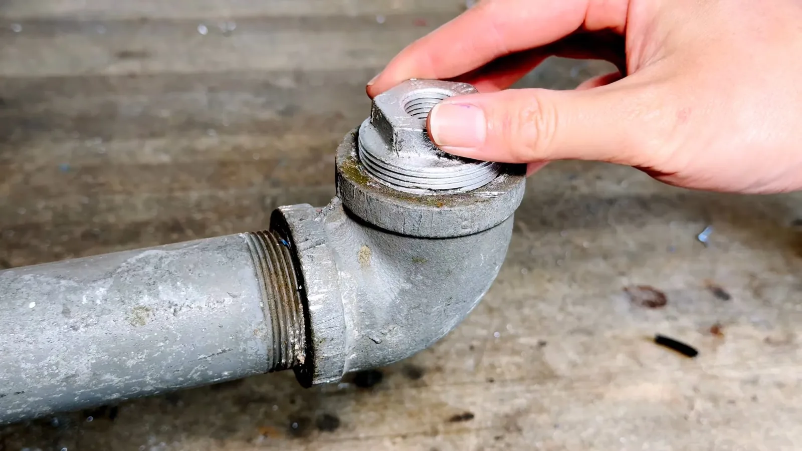 Hand loosening the cap on a galvanized cleanout fitting