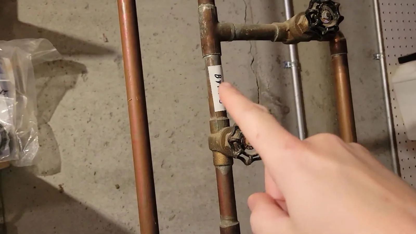 Finger pointing at a tagged shutoff valve on a copper water line