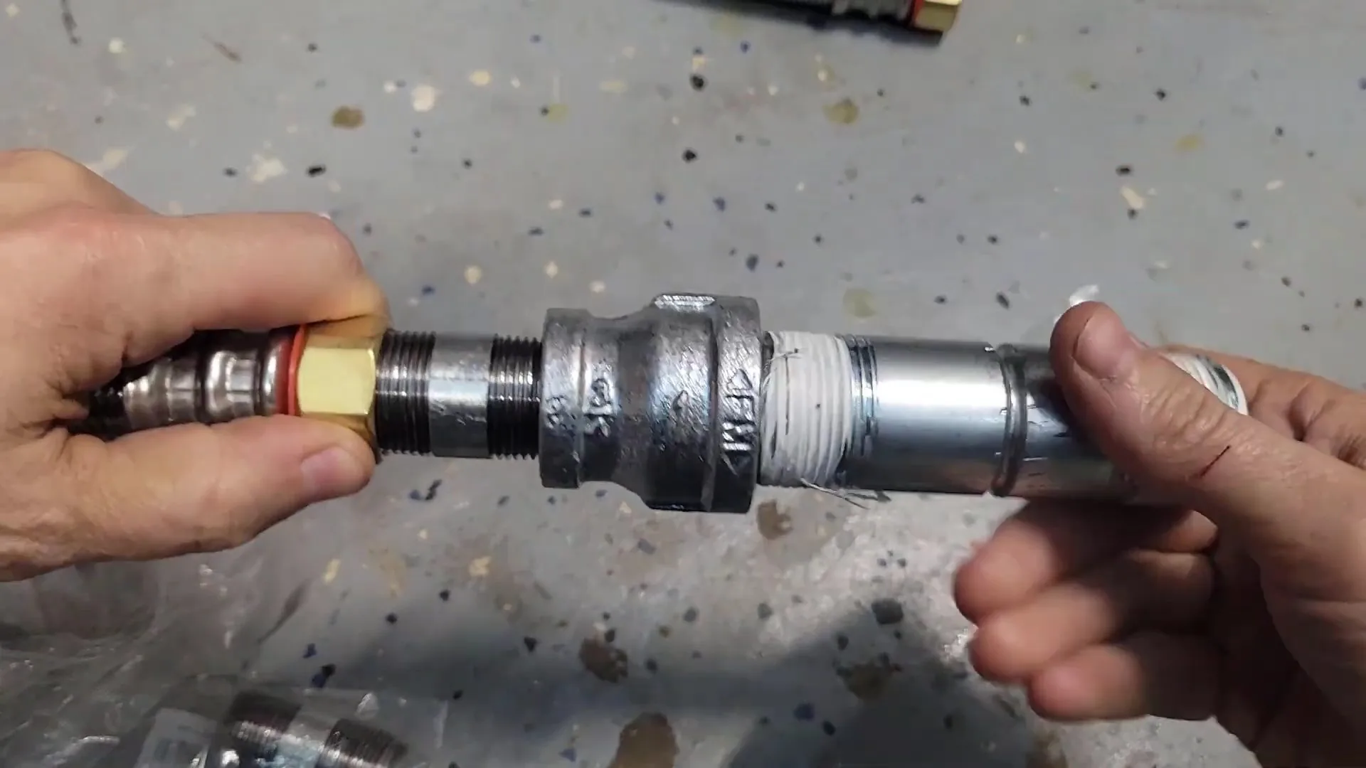 Two hands holding a threaded galvanized fitting assembly joined to a stainless flexible connector
