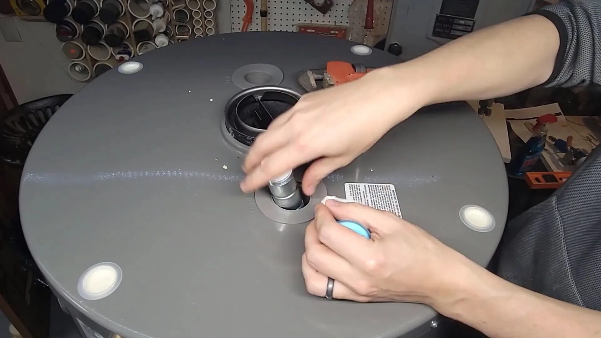Two hands tightening a pipe fitting on the gray top of a tank water heater