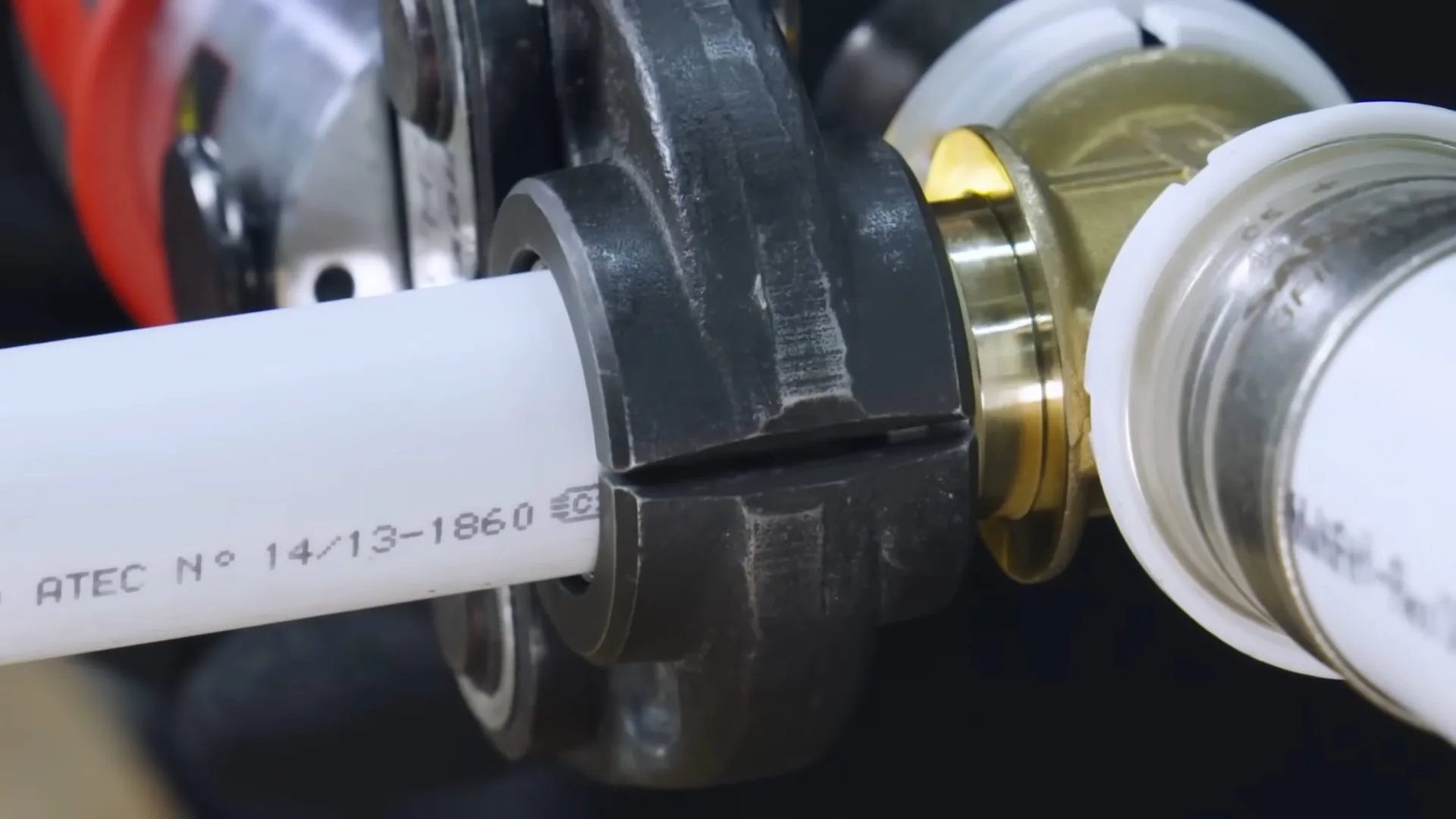 Close view of press tool jaws clamped on a white pipe where it meets a brass fitting