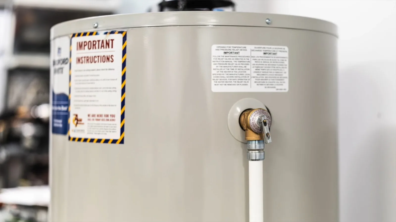 Warning and instruction labels on a tank water heater beside its temperature and pressure relief valve