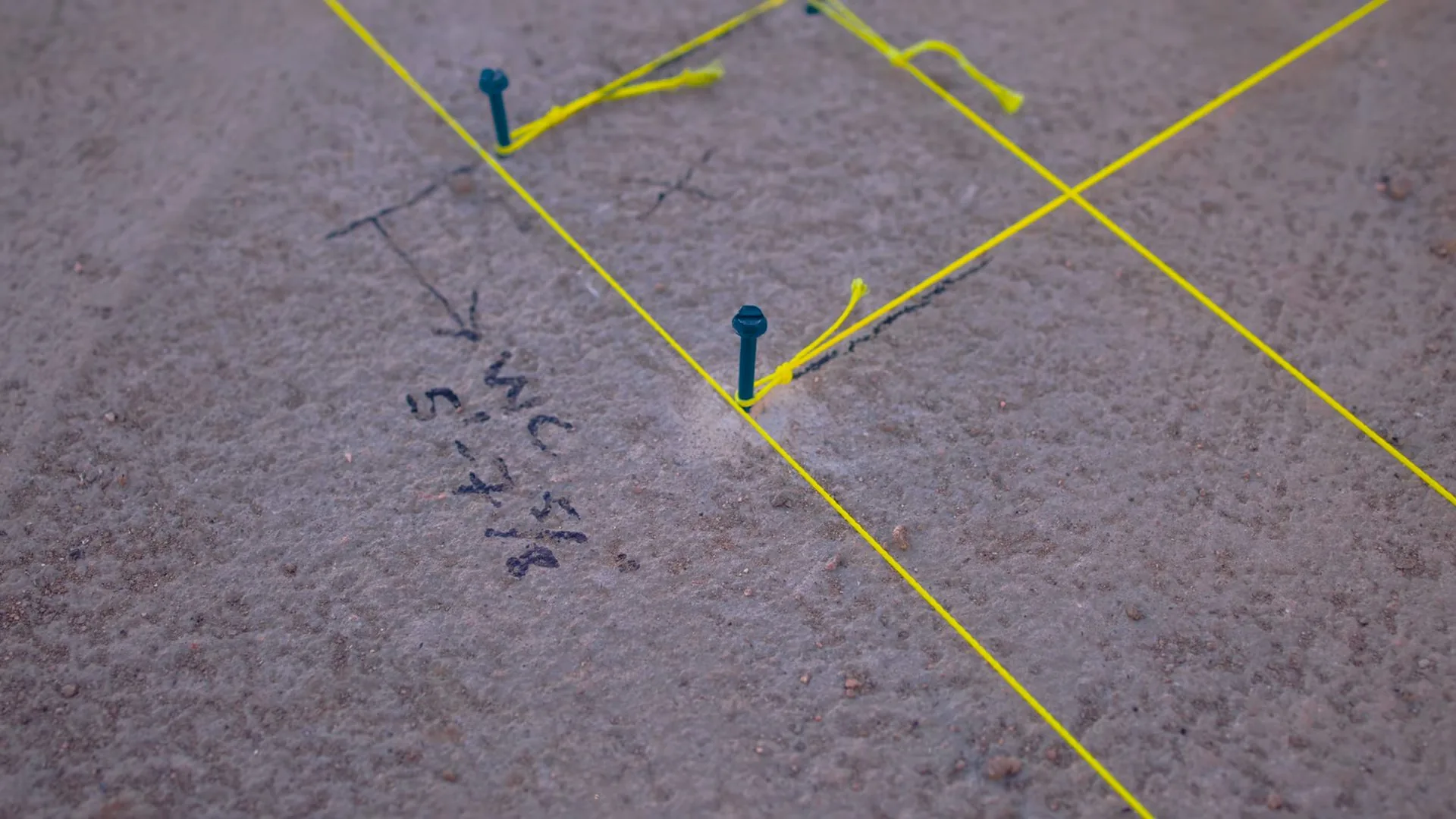 Yellow string lines and pins forming a marked grid on a floor surface with handwritten notes beside them